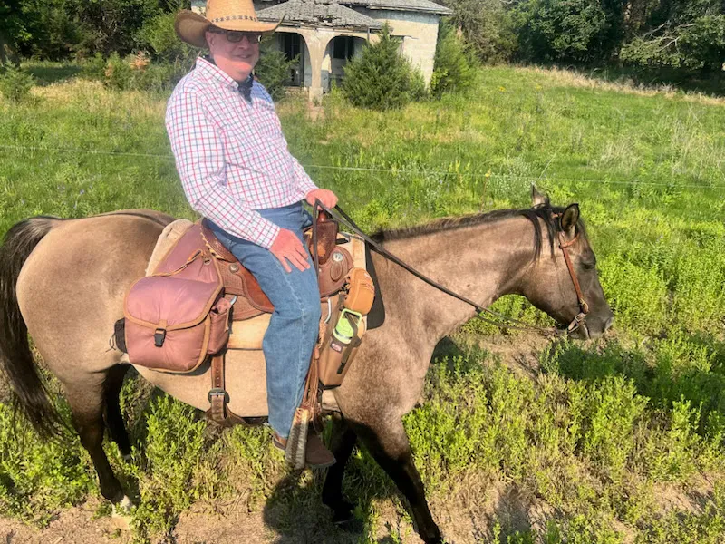Me in a straw cowboy hat, sitting on a dun horse in a green pasture at Rowse's 1+1 Ranch.