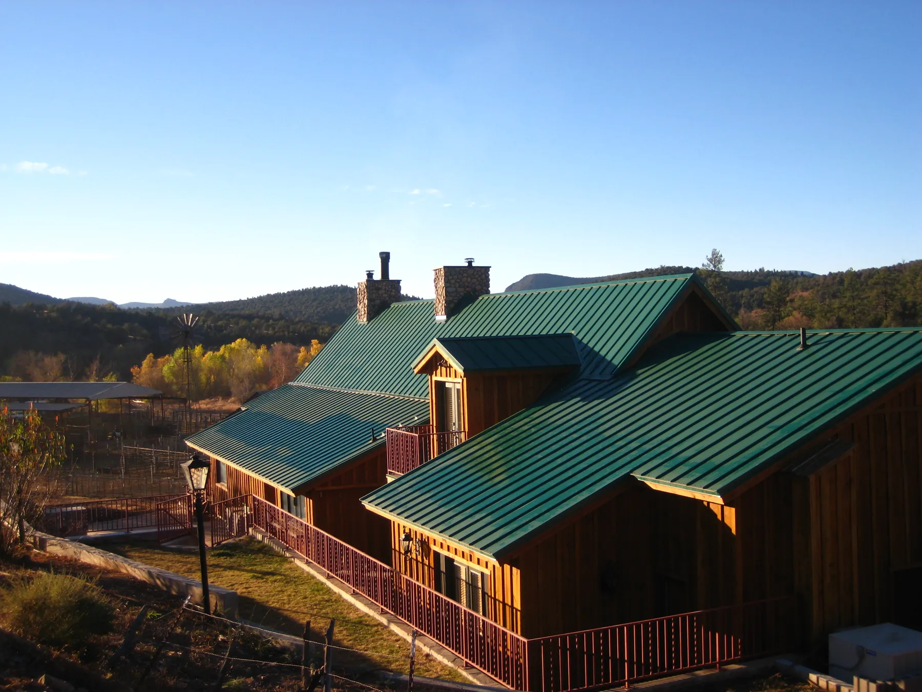 A board-and-batten lodge with green metal roofs and stone chimneys, with fall cottonwoods and hills behind.