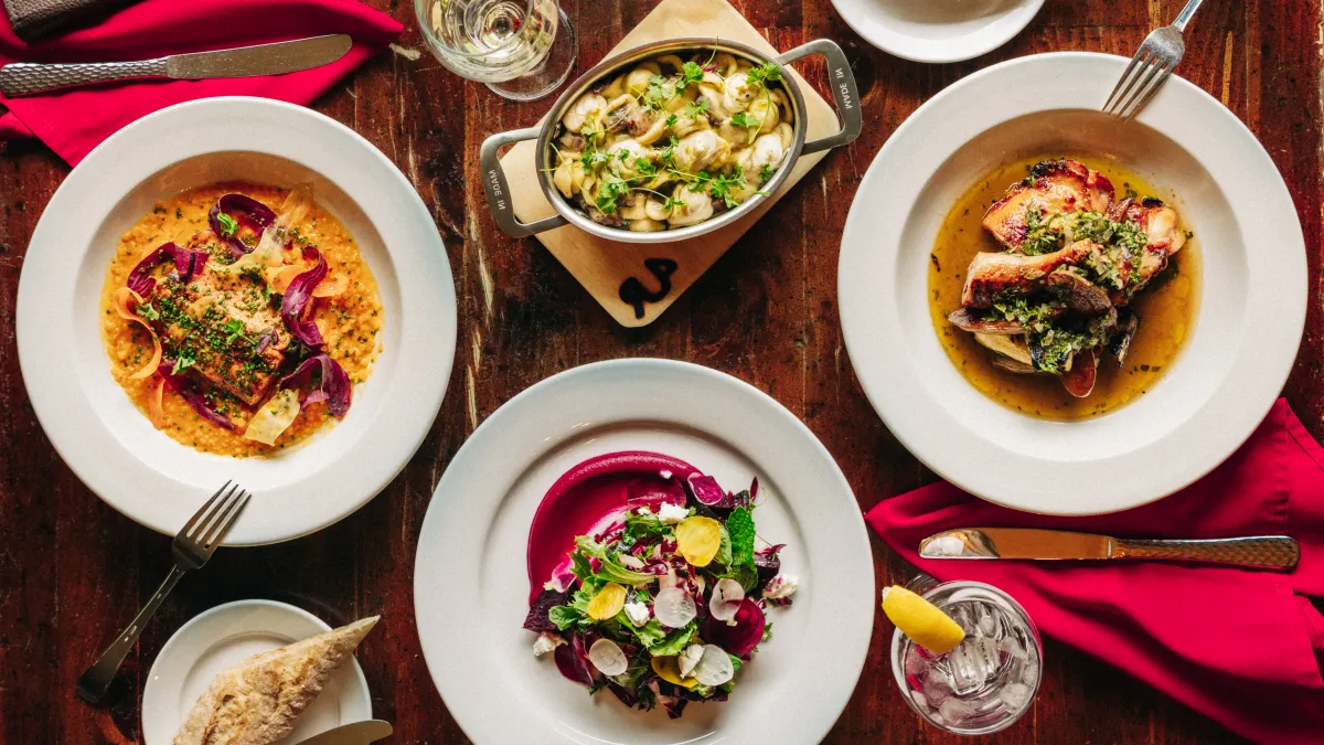 Four plated dinners and a skillet of pasta on a wooden table with red napkins.