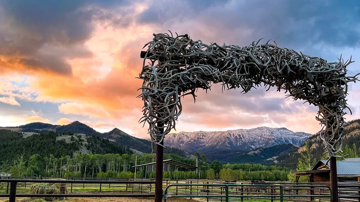 An arch of antlers over the corral gate, under a pink and orange sunset.
