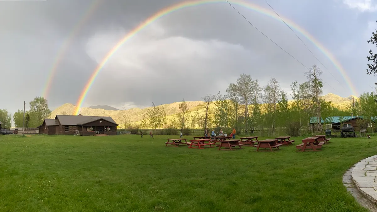 A double rainbow over the ranch lawn, picnic tables and log cabins.
