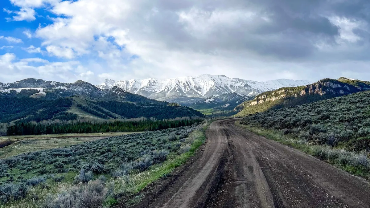 A dirt road running through sagebrush toward snow-capped mountains.
