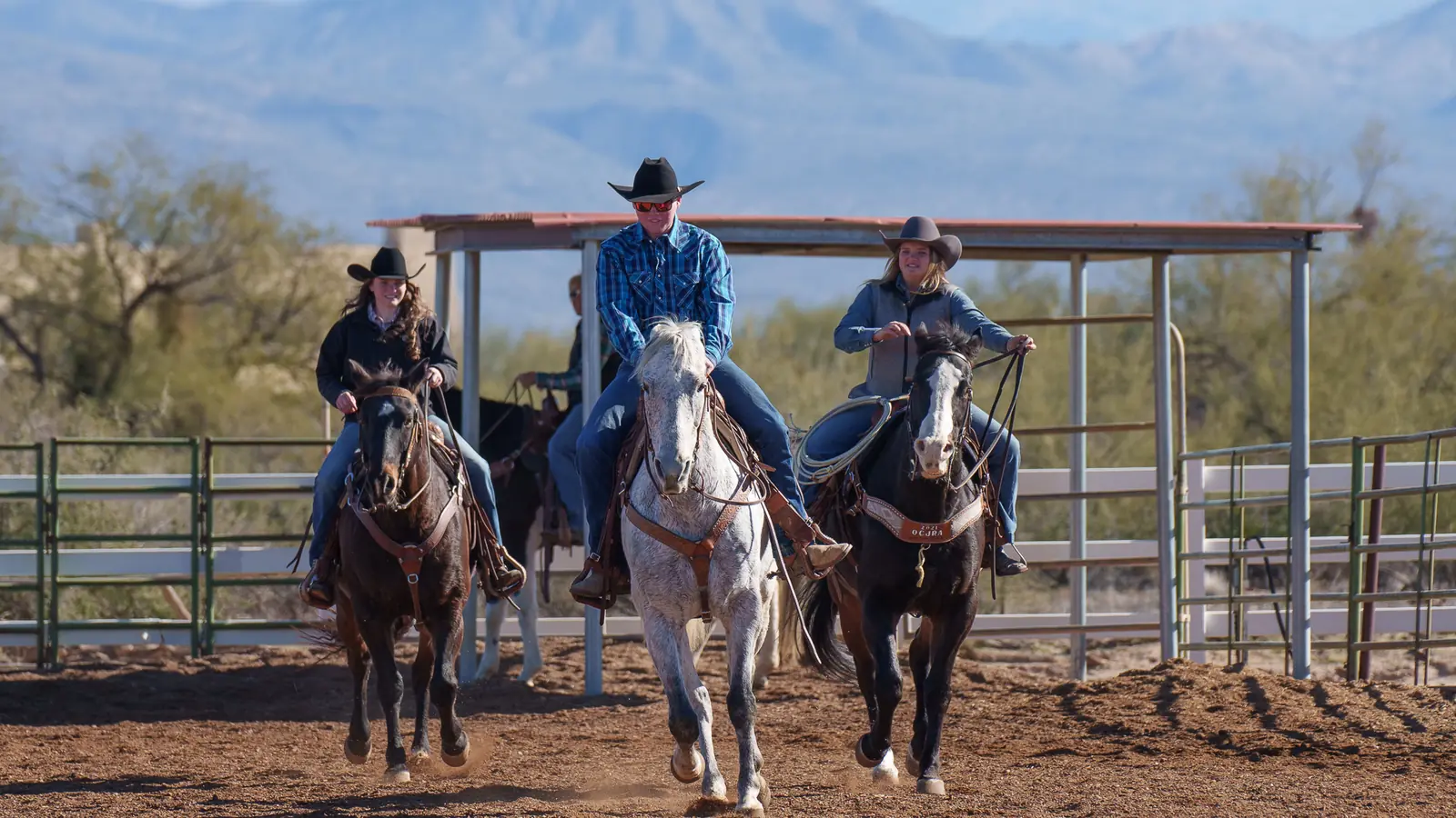 Three riders walking their horses out of a desert arena below distant mountains.