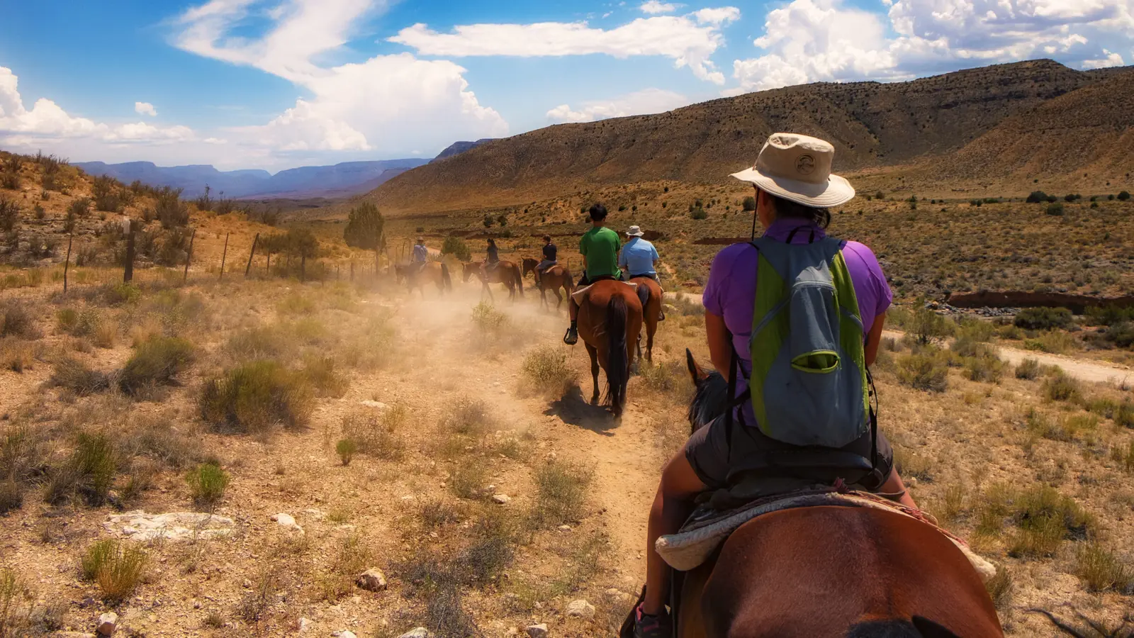 A line of riders following a dusty trail through Arizona Strip desert hills.