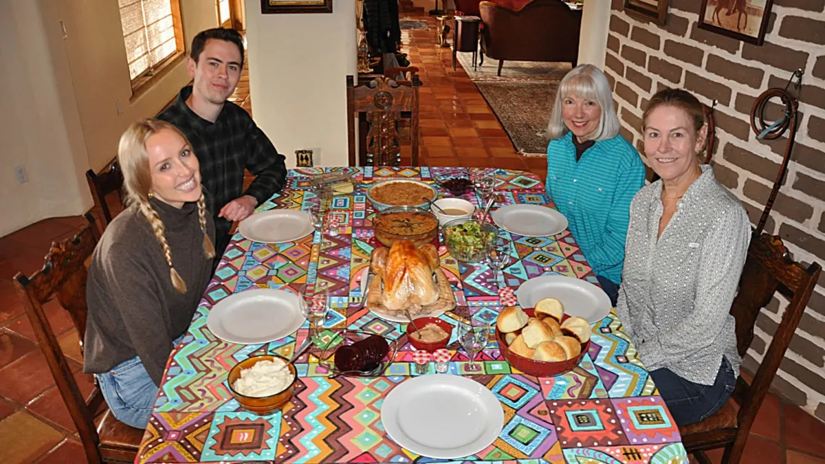Four guests smiling around a supper table set with a bright patterned cloth.