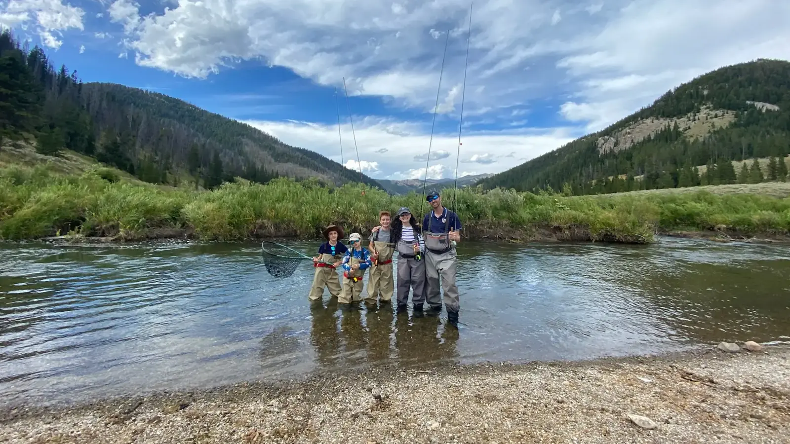 Guests fly fishing together in a mountain river in a green valley.