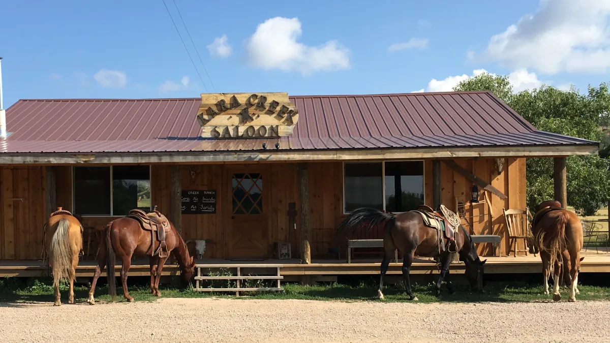 Four saddled horses grazing in front of the Kara Creek Saloon's log porch.