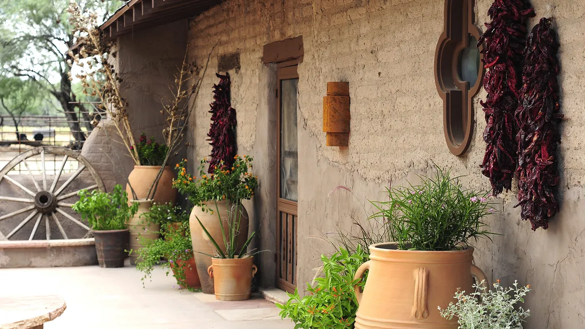 An adobe wall with chile ristras, clay pots and a wagon wheel.