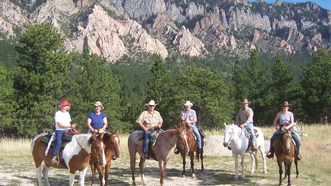 Six guests on horseback lined up below tall granite cliffs.