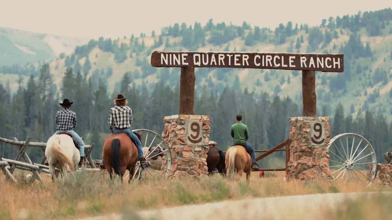 Riders on horseback at the stone entrance gate of Nine Quarter Circle Ranch.