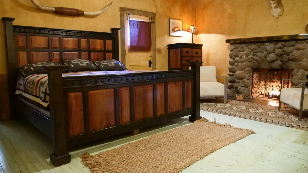A guest room with a carved wooden bed, a stone fireplace and longhorns on the wall.