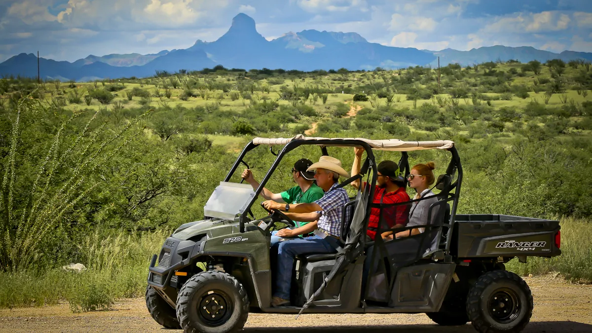 Guests in a UTV on a dirt road, with Baboquivari Peak in the distance.