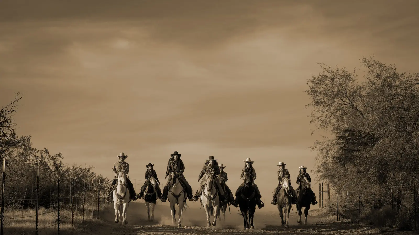 A sepia photo of a line of riders heading out across the desert.