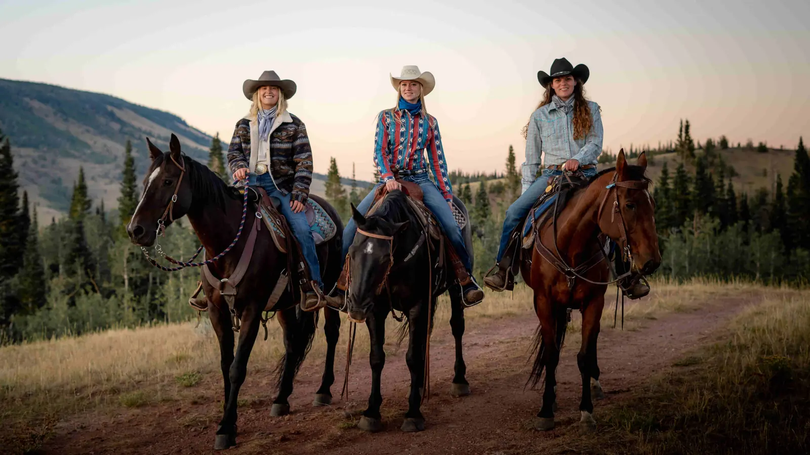 Three riders in cowboy hats on horseback on a mountain trail.