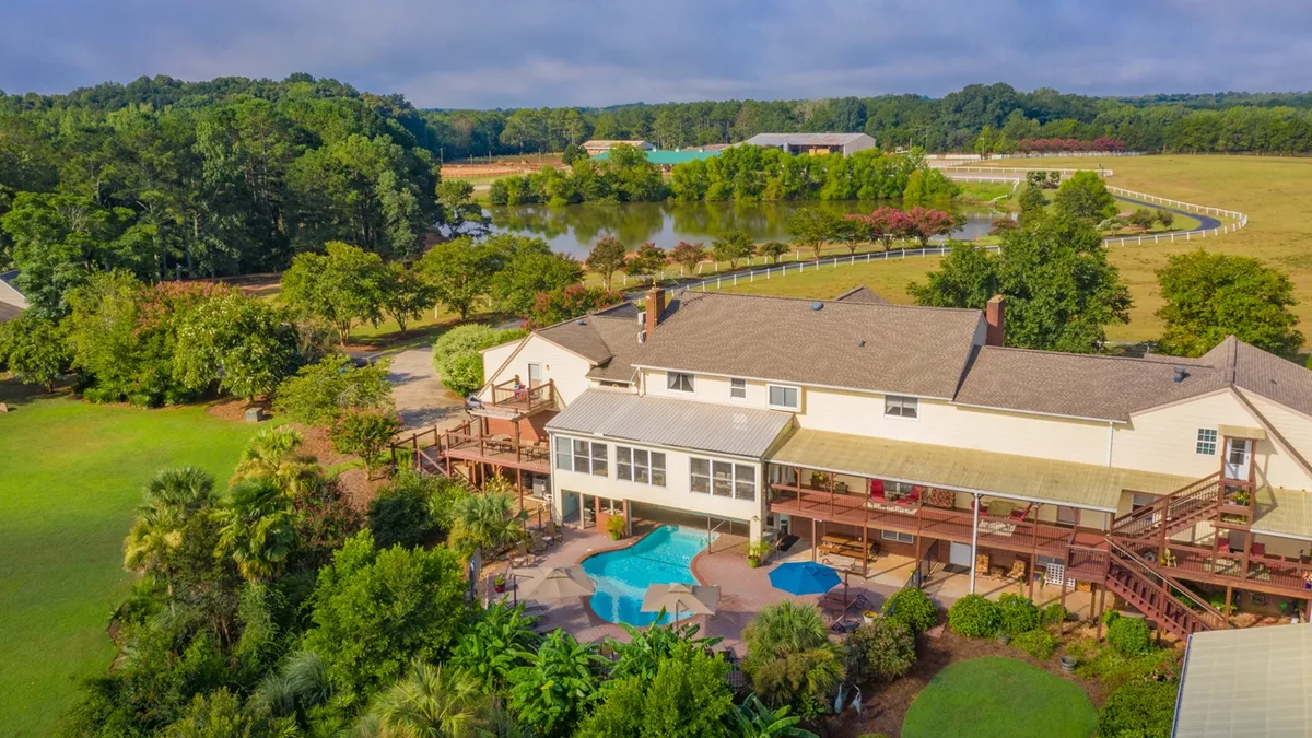 The lodge with its decks and pool, above a pond and fenced pastures.