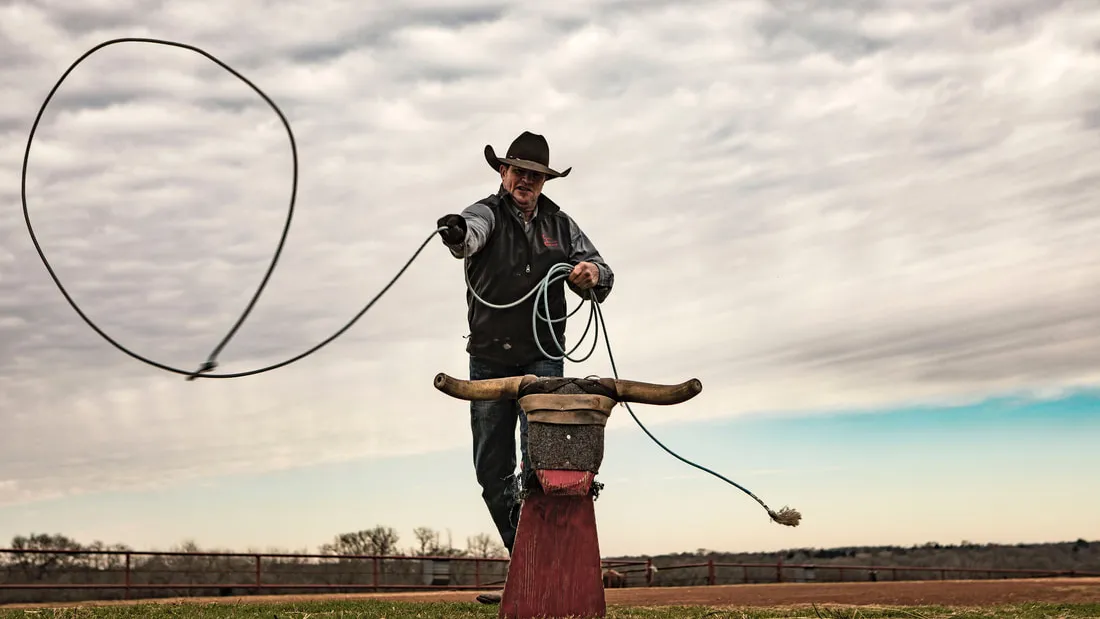 A cowboy throwing a loop at a roping dummy under a cloudy sky.