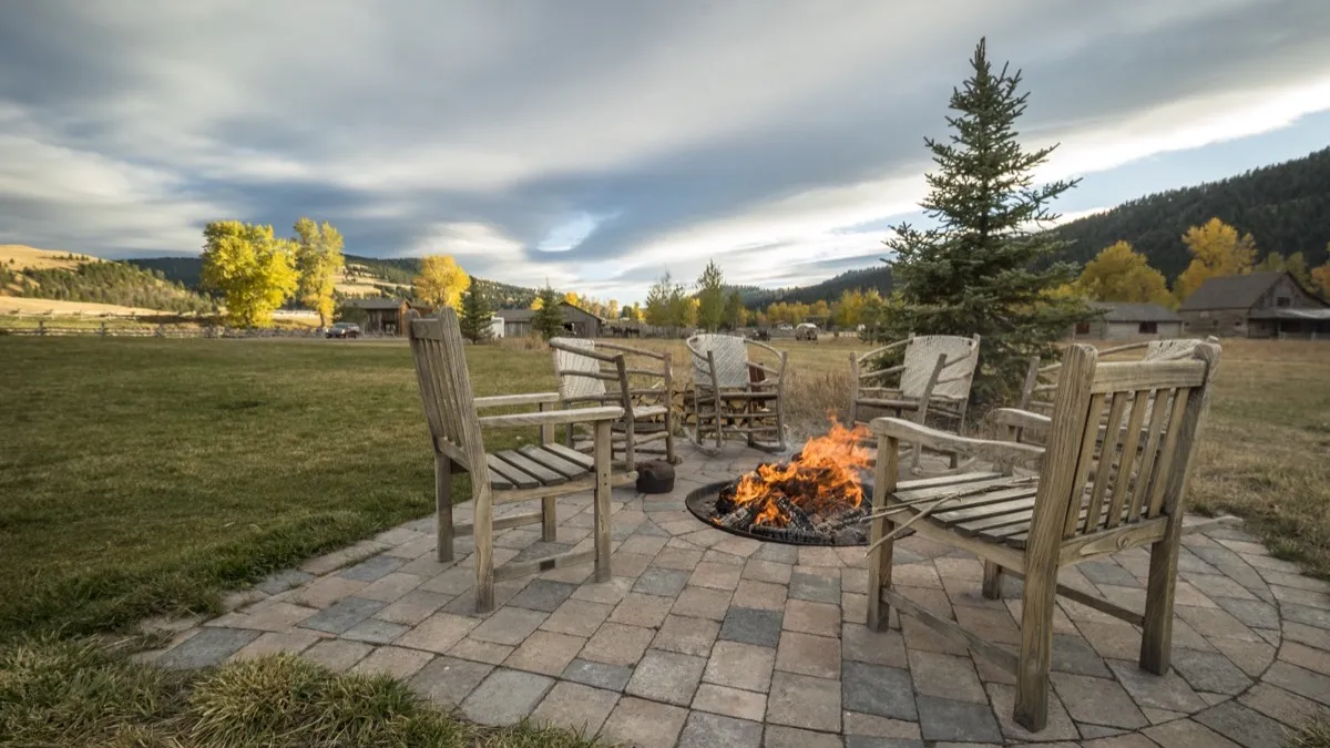 Wooden chairs around a fire pit on a stone patio, with fall aspens and ranch buildings behind.