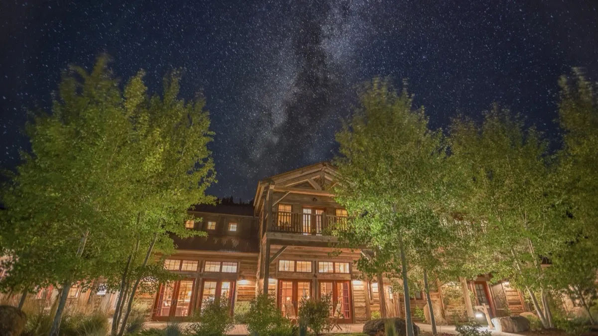The Granite Lodge lit up under the Milky Way, framed by aspens.