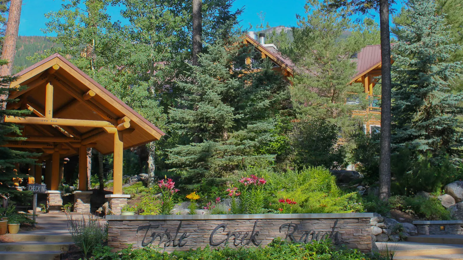 The log lodge entrance at Triple Creek Ranch, with flower beds and tall pines.