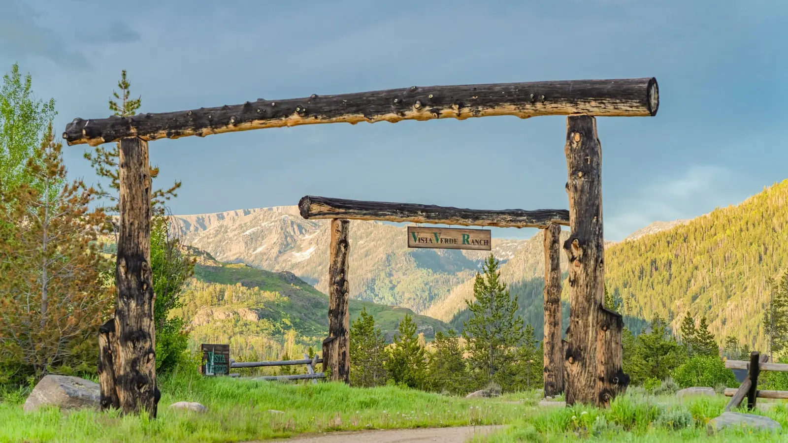 The log entrance gate of Vista Verde Ranch with green mountains behind it.
