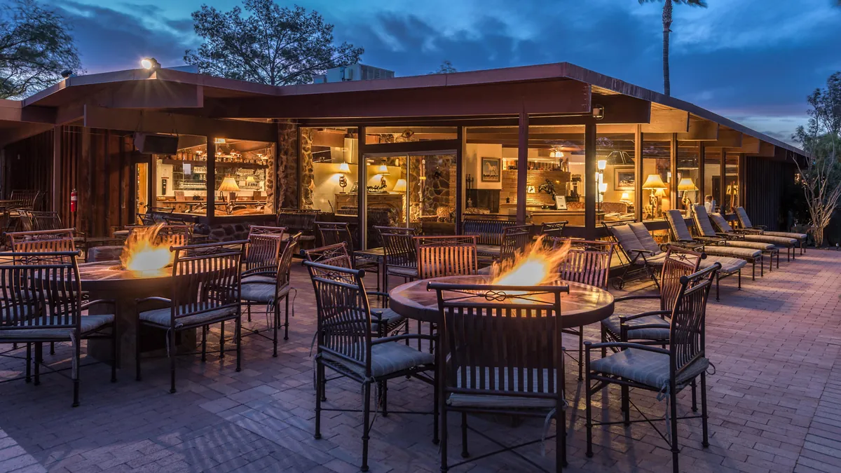 A patio with fire tables and chairs outside the lit lodge at dusk.