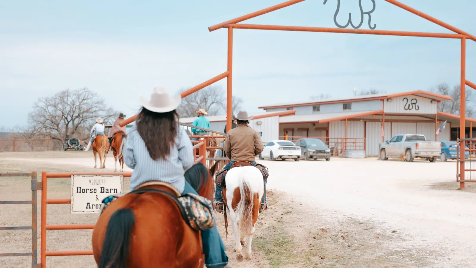 Riders heading under the orange Wildcatter brand gate toward the horse barn and arena.