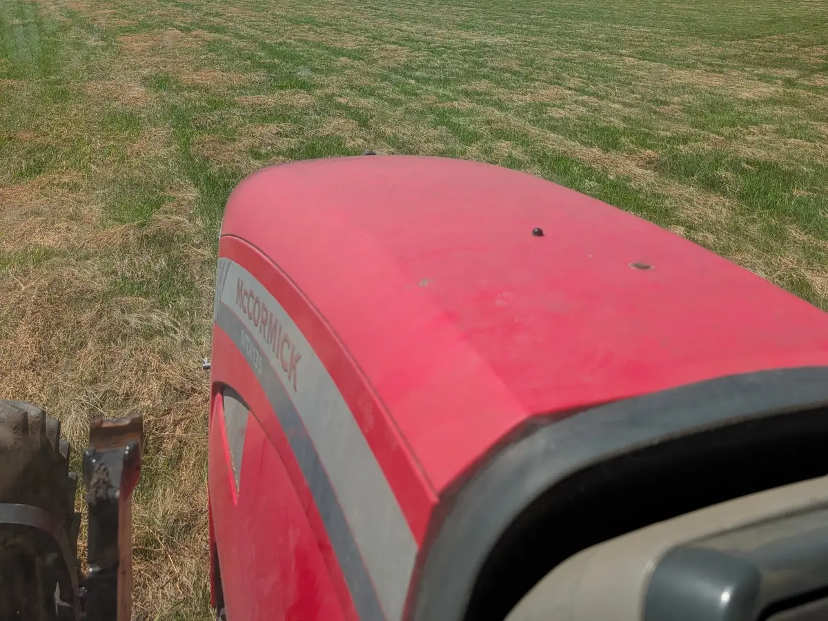A raked hayfield seen over the red hood of a tractor.