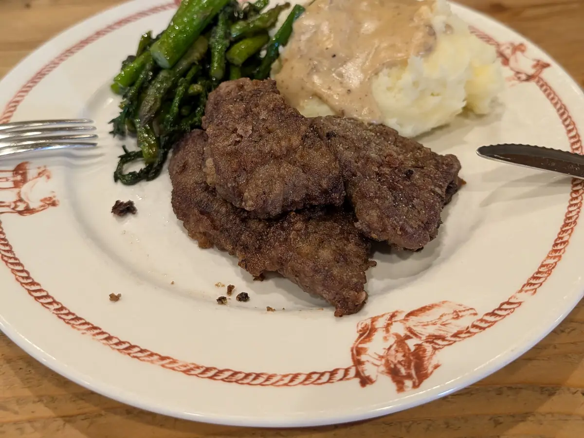 A dinner plate of steak, mashed potatoes with gravy and green beans.
